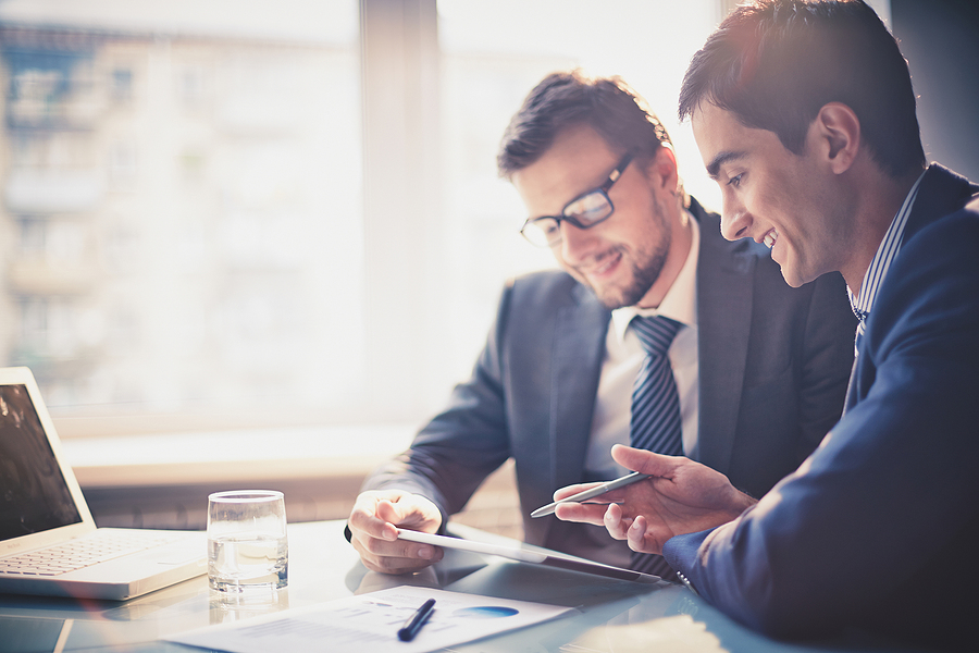 Two businessmen reviewing data on a tablet during a professional meeting.