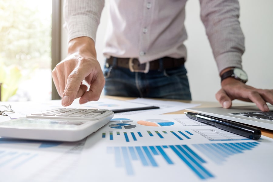 Person using a calculator with charts and graphs on a desk