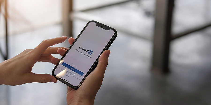Hands holding a smartphone displaying the LinkedIn login screen.