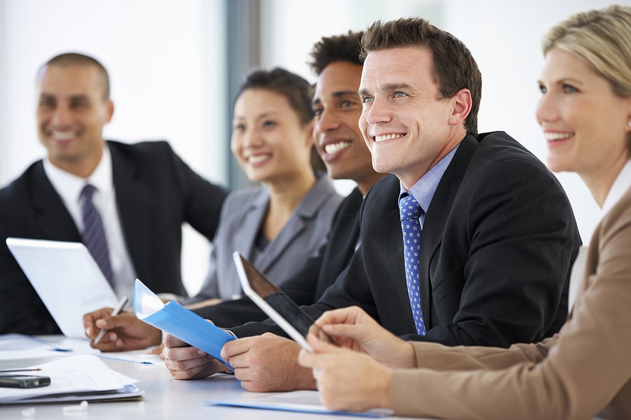 Group of business professionals smiling during a meeting, holding documents and tablets.