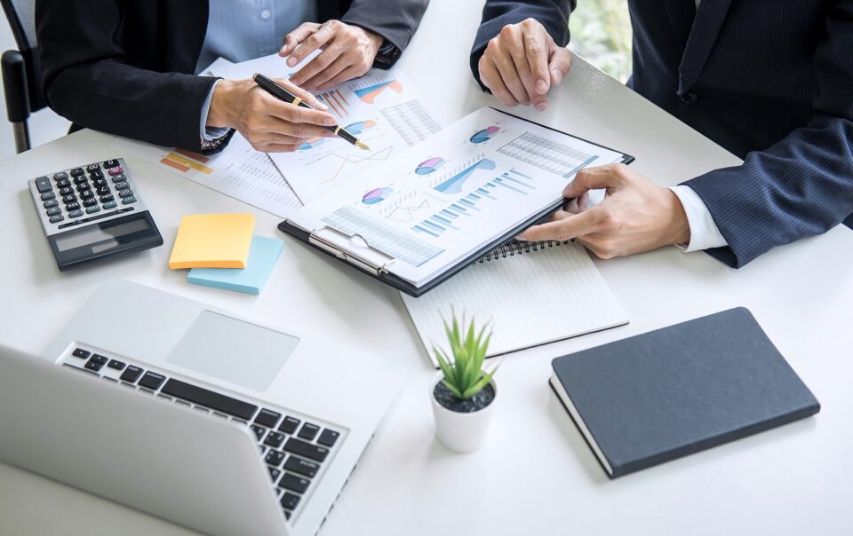 Business colleagues reviewing financial charts and graphs on a table with documents, calculator, and laptop.