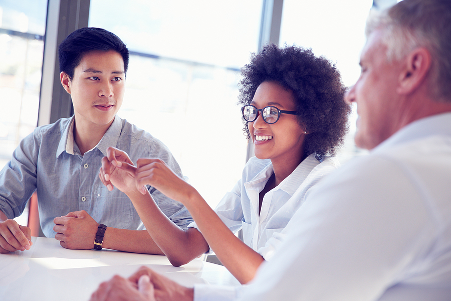 A group of three business professionals engaged in a discussion at a bright office table.