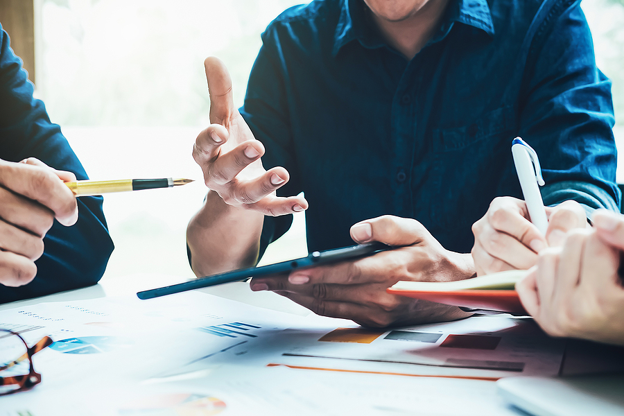 Close-up of hands discussing business data with a tablet and documents on a table.