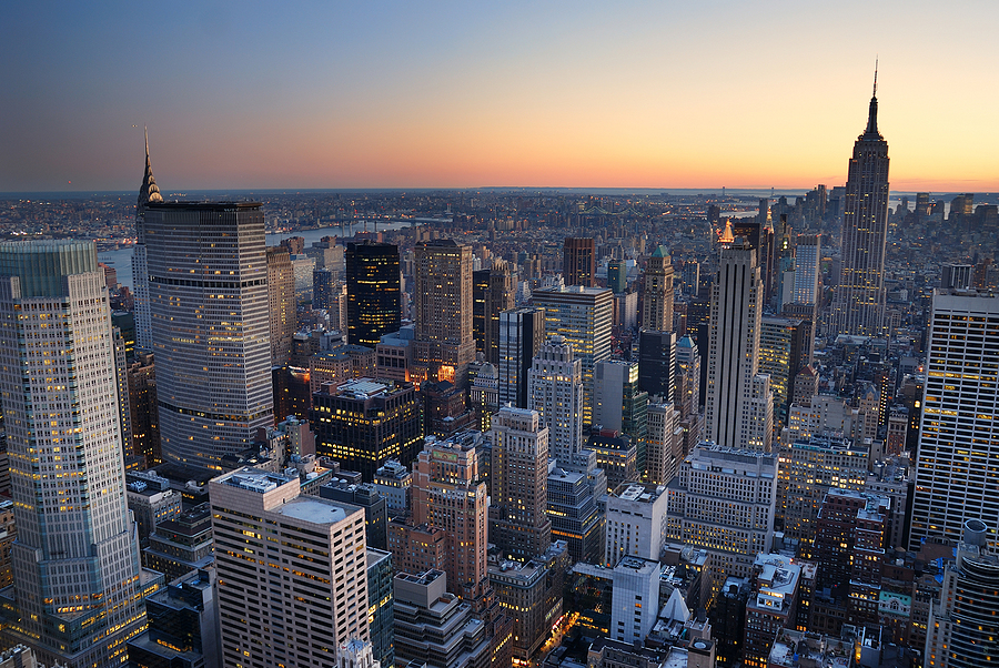 Aerial view of New York City skyscrapers at sunset with a colorful horizon.