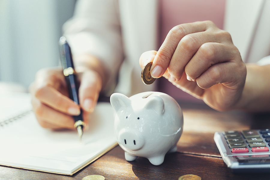 Businesswoman dropping a coin into a piggy bank while writing financial notes.