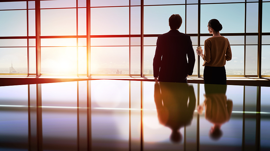 Business professionals overlooking a cityscape through large windows during sunset.