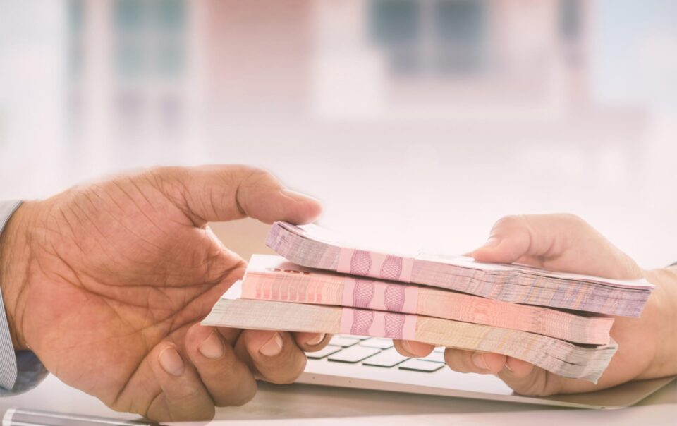 Hands exchanging cash over a contract, symbolizing business loans and financial support for growth.